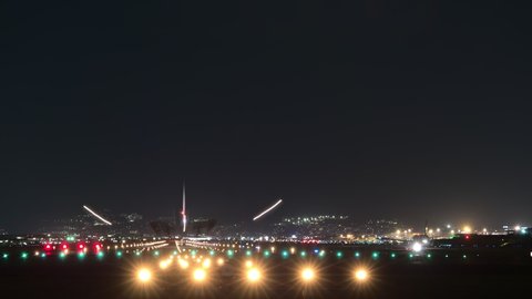 Time lapse shot of airport runway at night hour. Planes quickly arrive and departure. Bright edge and approaching lights on ground, dark sky. Motion blur silhouettes of airliners