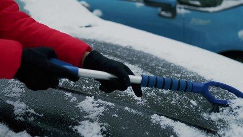 Woman hands cleans the car of snow with a brush. Snowfall covered the car. Slow motion