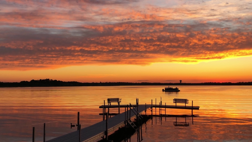 Beautiful Lake Irving in Bemidji Minnesota, the first lake on the Mississippi River, is seen at sunset as a pontoon with fishermen floats past a boat dock on a calm evening.