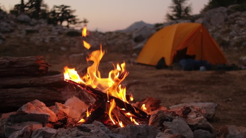 Bonfire burning in tourist camp in mountains. Beautiful campfire, burning wood by tent in summer evening. Active lifestyle, traveling, hiking and camping concept. Campfire burning in slow motion Royalty-Free Stock Footage #1063958446