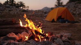 Bonfire burning in tourist camp in mountains. Beautiful campfire, burning wood by tent in summer evening. Active lifestyle, traveling, hiking and camping concept. Campfire burning in slow motion - Powered by Shutterstock - Get 15% off with code: PIKWIZARD15
