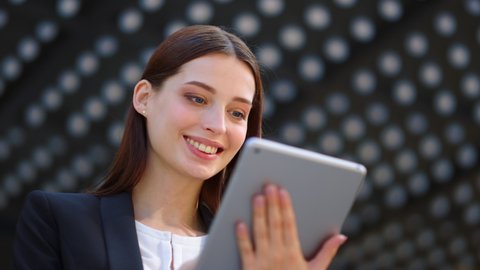 Closeup happy woman face looking tablet screen outdoors. Elegant businesswoman chatting online with digital device outside. Portrait of business woman using tablet computer near office building.