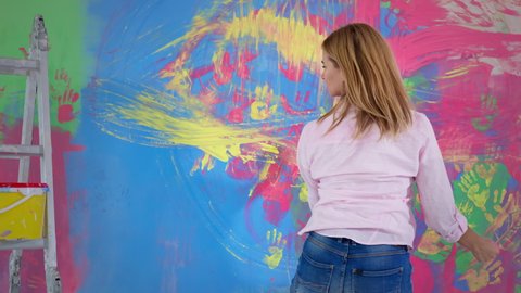 active female artist using fingers she creates colorful, emotional and sensual painting, girl draws with her hands on the wall, rear view