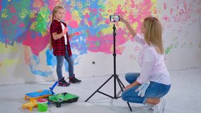 mom and daughter vlogging, child girl with colorful palms waves hands on smartphone camera and shows thumbs up during renovation