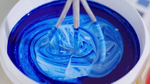 mixing building materials for painting walls, worker mixes blue and white paint in bucket with whisk and drill to renovate room, close-up