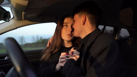 Cheerful young man smiling and embracing girlfriend while sitting inside vehicle