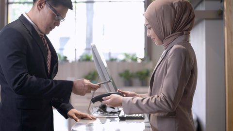 Beautiful asian woman seller receive a payment from business man which using smartphone scanning at counter lobby. Concept technology device digital payment and shopping with contactless.