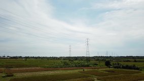 Aerial drone view of a newly constructed electric transmission tower on a green rice field at the sunset.