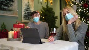 Couples sit in front of their laptops with Corona masks at Christmas and arena a bad mood and bored during a video call