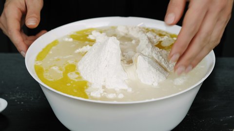 Hand is mixing ingredients for yeast dough in bowl at modern professional kitchen. Baker is mixing flour, water and olive oil in bowl cooking dough for pizza