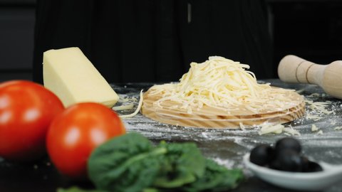 Grated cheese flakes are falling on black wooden table filled with cheese. Cookery concept. Process of making pizza
