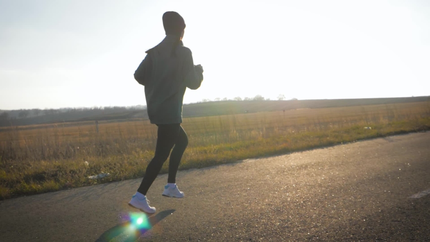 Young fitness sport woman running on road at sunset. Athlete runner feet running on road, slow motion.