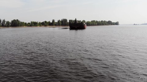 Empty cargo ship in the middle of the river in the evening. The copter flies to the ship from afar. Transportation of cargo along the river.
