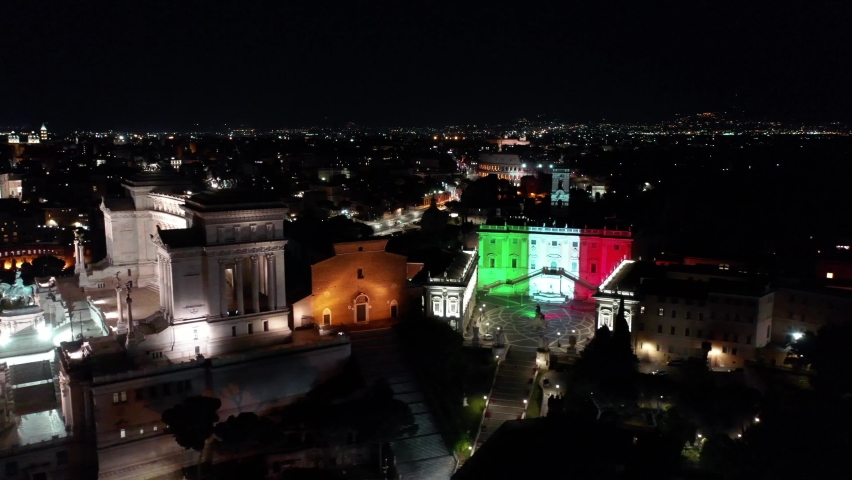 Italian flag illuminates the facade of the Capitol. Aerial view with drone on Alatre della Patria and the Imperial Forums. Night. Center city of Roma, Italy.