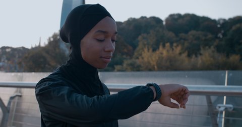 Crop view of attractive muslim woman in sports suit looking at smart watch. Beautiful young female person in hijab started running after break. Concept of healthy lifestyle, sport.