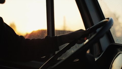 Close-up of a young man's hand on the steering wheel of a car on the background of sunset outside the window cabin