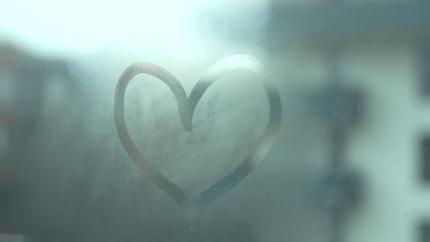 Hand erasing destroys heart shape drawing on misted window in a dark environment. Breakup, broken heart and relationship problems. Love is over concept. Selective focus. Royalty-Free Stock Footage #1063986385
