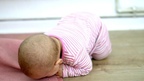 Adorable baby lying face down on wooden floor and biting pink foam mat. Curious baby playing on the floor. Happy babies having fun