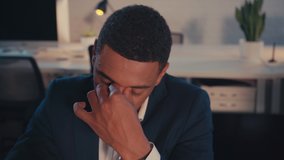 tired african american businessman touching eyes in office at night