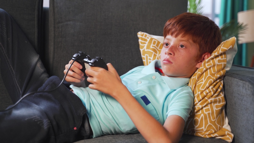 Alone young kid playing video game using joystick during late night while sleeping on bed - concept of kids game addiction and late night playing games | Shutterstock HD Video #1063987630