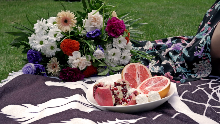 Romantic picnic on the green grass. Flowers, fruits. Woman