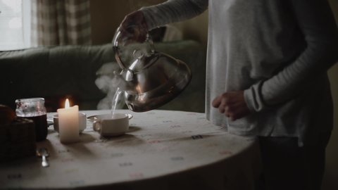 Woman pours hot tea from a teapot into a cup