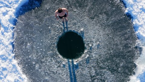 Winter swim. Young man jumps into winter lake at sunny day. Multi camera scene. Camera 3. Aerial, top down view