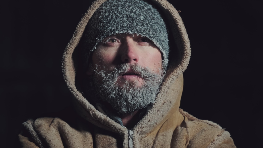 Man with frozen face. Young adult man with icy beard and hat breathes outdoor at subzero temperatures environment