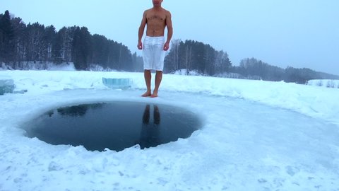Young man with lean body jumps into the ice hole and haves recreational winter swim