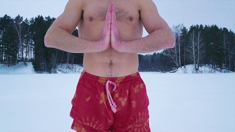 Young man in the red colorful pants meditates standing in the snow with winter forest on the background. Fast dolly out camera (drone)