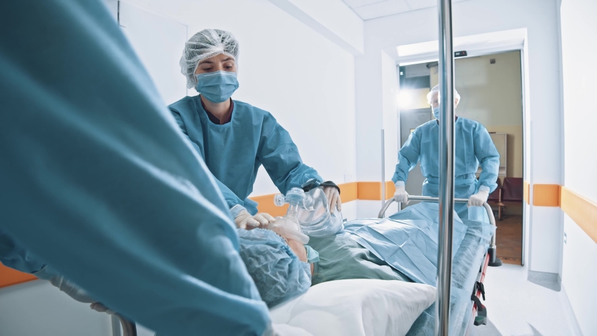 Emergency department. skillful doctors, nurses and surgeons moving seriously injured patient with oxygen mask lying on stretcher through hospital corridors. Reanimation and medicine concept Royalty-Free Stock Footage #1063997419