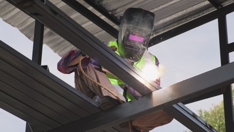 Asian male welder is welding steel beams in process of home renovation. Man worker working for building construction and structure. Professional labor occupation concept.