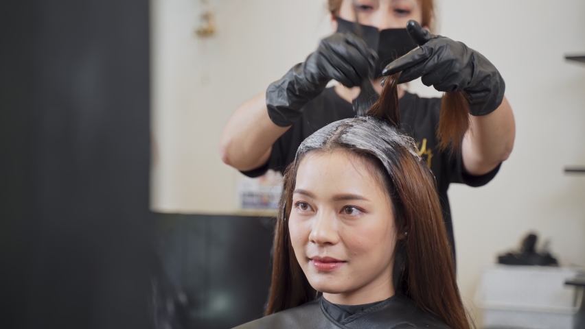 Young Asian beautiful girl changing hairstyle and color in salon. Hairdresser dyeing woman customer hair in the beauty shop. The woman looking at mirror with smile face. Hair beauty and salon concept. | Shutterstock HD Video #1063999126