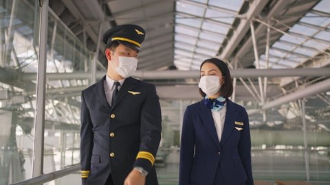 Airliner pilot and air hostess wearing face mask walking in airport terminal to the airplane during the COVID pandemic to prevent coronavirus infection. New normal lifestyle in air transport concept.