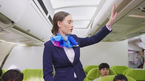 Beautiful Caucasian flight attendant walking on aislel to close luggage compartment and check the readiness of airplane before take off. Safety check procedure of cabin crew in the plane.