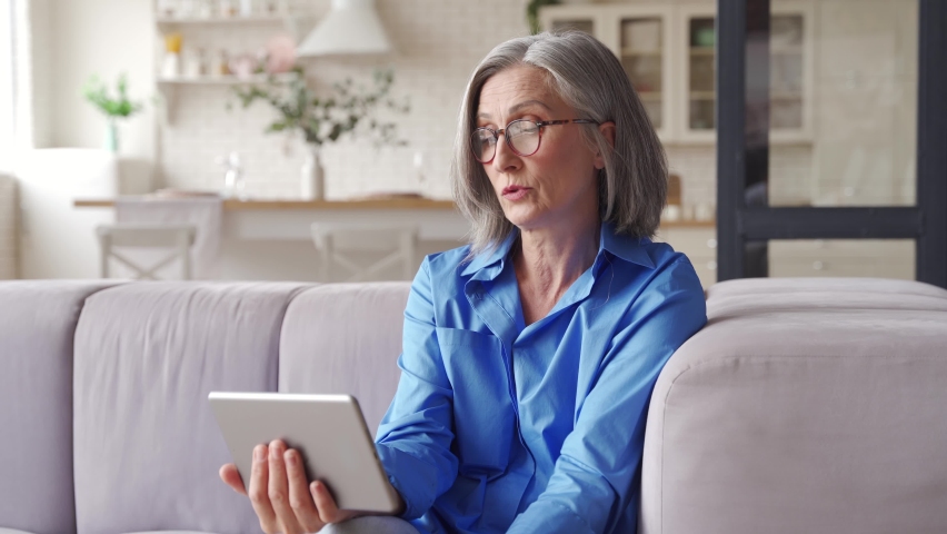 Senior old grey-haired woman grandmother holding digital tablet video conference calling talking with doctor or family during social distance virtual visit in online telemedicine chat meeting at home. | Shutterstock HD Video #1064001616