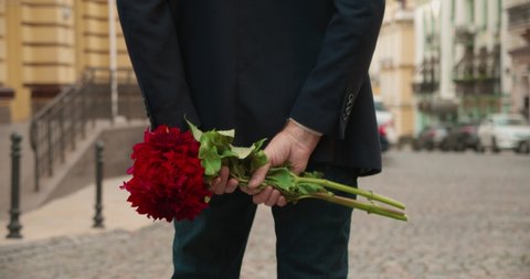 Male hands holding red flowers bouquet behind back, man waiting for girlfriend