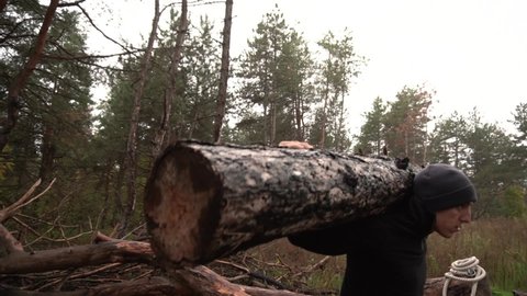 Close-up. A man goes in for sports at the edge of the forest in black pants, a sweatshirt, a hat. Crossfit squatting with a heavy log. In autumn, cloudy and cold. The camera moves around