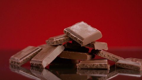 Bunch of chocolate pieces. Stock footage. Close-up of hand taking piece of chocolate from pile on isolated background. Pile of chocolate bar pieces. Delicious chocolate bars. Sweet tooth 