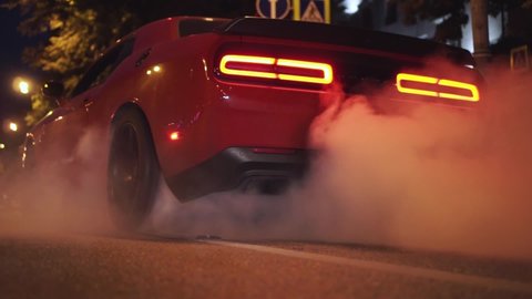 Car start with smoke on wheels. Footage. Red modern drag sport auto burning tire at city street.