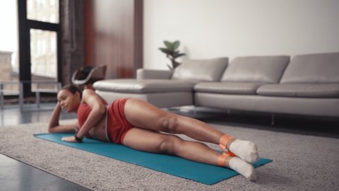 Afro american young sportive woman doing leg exercises using fitness elastic bands while lying on a sports mat at home.