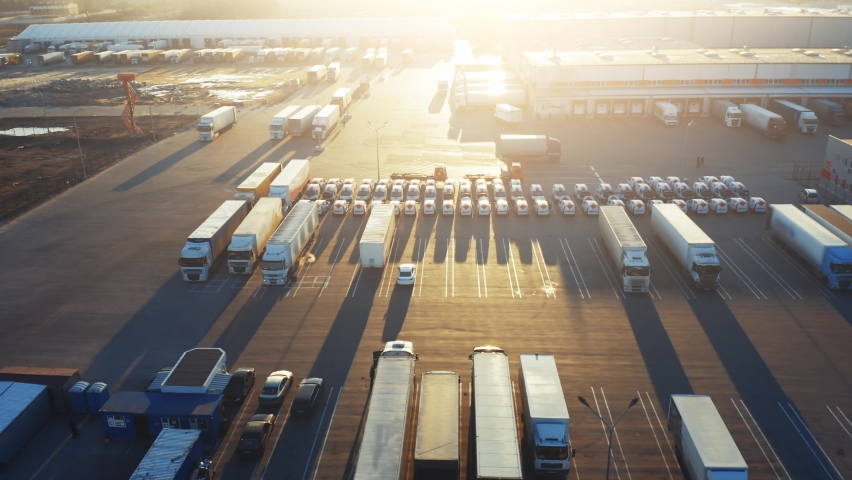 Semi-trailer trucks stand on the parking lot of the logistics park with loading hub and wait for load and unload goods at warehouse ramps at sunset. Aerial view | Shutterstock HD Video #1064014351