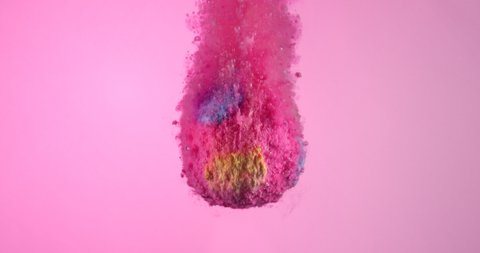 Pink colorful bath bomb falling down into clean water in slow motion against light pink background.