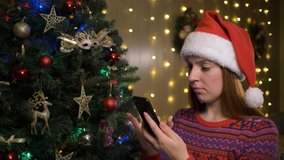 Portrait of young beautiful woman with santa hat in winter sweater typing message on mobile phone and reacting emotionally receiving good news. - Powered by Shutterstock - Get 15% off with code: PIKWIZARD15