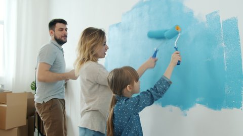 Happy family dad mum and child enjoying apartment renovation painting wall and dancing having fun together. Leisure time activities and housing concept.