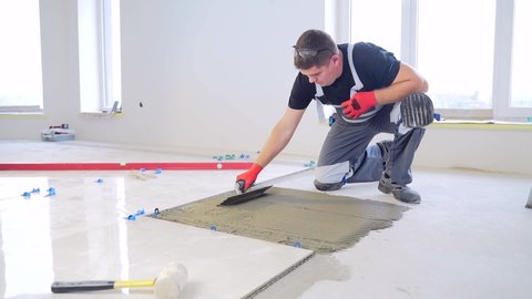 Construction repairs laying of a ceramic tile on a concrete floor with use of tool and glue mixes. Worker repairman Man builder master, notched trowel putting tiles adhesive mix with notched trowel