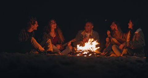 Group of friends singing playing ukulele at beach night bonfire
