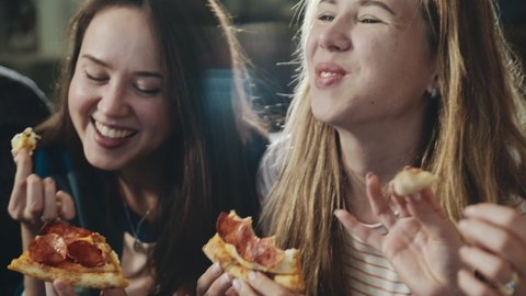 Happy group of friends sharing pizza. Everybody laughing, chatting having great time together. One girl stealing piece from friend. Concept of millenials, lifestyle, indoors leisure, food.