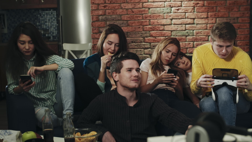 A group of teenagers bored in home party. Millennials using their smartphones, gadgets, not interacting with each other. Showing lack of social interaction. Concept of phubbing, boredom, technology. | Shutterstock HD Video #1064025934
