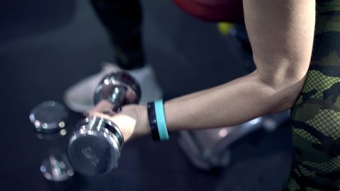 Close-up raised arms of middle-aged woman lifting dumbbells. Lady of thirty training her body in gym. Active woman exercising in fitness hall. Woman doing sports and fitness training. Leisure concept.